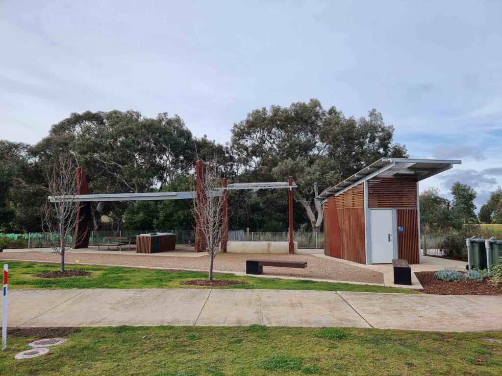 Grassy area, footpath and undercover bbqs and wood clad toilet block next to warralily boulevard playground